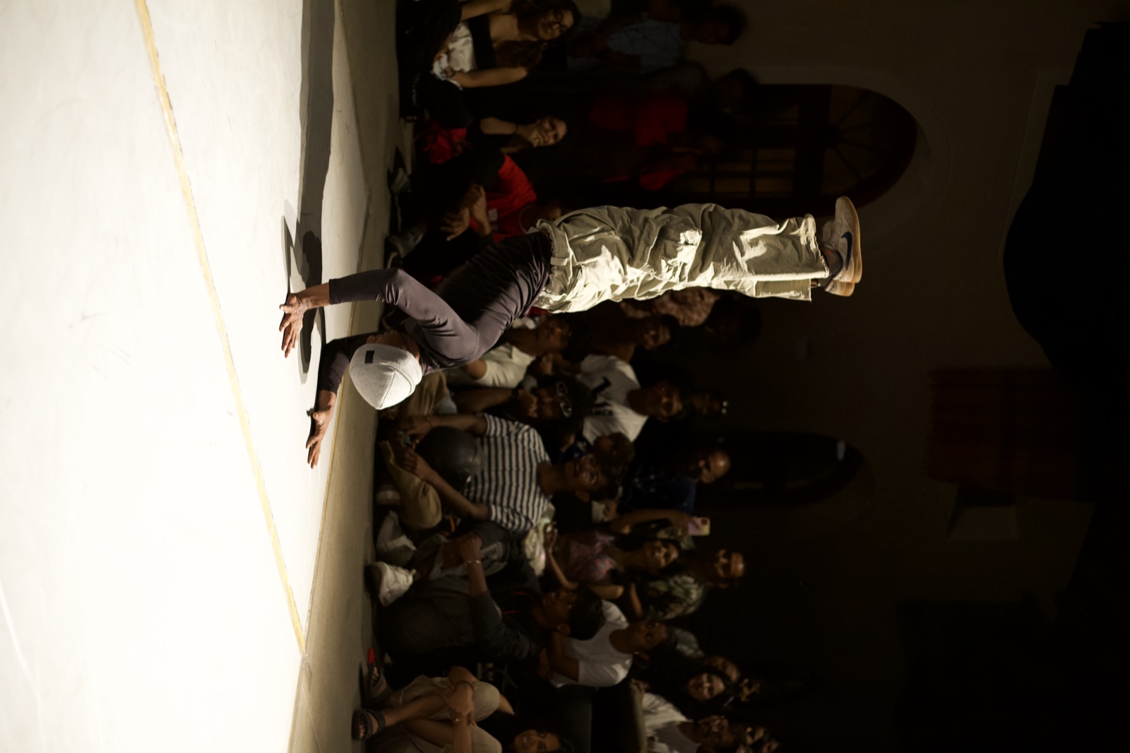 A breaker in a one-arm handstand, crowd watching from the dark